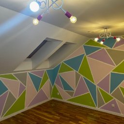 Budmar Marcin Garncarek - Pokój na poddaszu z geometrycznym wzorem na ścianie w odcieniach zieleni, błękitu, różu i szarości, oświetlony dwoma designerskimi lampami.