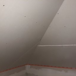 Budmar Marcin Garncarek - Montaż płyt gipsowo-kartonowych na poddaszu, widoczne otwory po wkrętach i taśma uszczelniająca na styku ściany i sufitu.