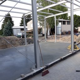 Budmar Marcin Garncarek - Wygładzona betonowa podłoga pod konstrukcją szkieletową budynku, widoczna zacieraczka do betonu i miotła oparta o słup.