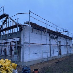 Budmar Marcin Garncarek - Budowa domu z betonu komórkowego w Ostrowie Wielkopolskim, widoczne rusztowania i konstrukcja dachu w trakcie montażu, niebieskie niebo w tle.