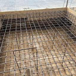 Budmar Marcin Garncarek - Zbrojenie fundamentów domu jednorodzinnego w szalunku z płyty OSB, widok z góry, siatka z prętów stalowych ułożona na betonowej podstawie.