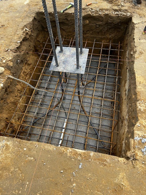 Zbrojenie fundamentu z wystającymi prętami i stalową płytą kotwiącą, umieszczone w wykopie.