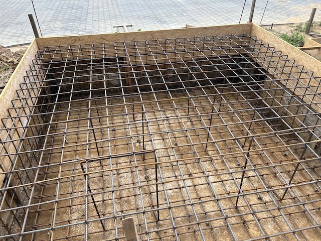 Zbrojenie fundamentów domu jednorodzinnego w szalunku z płyty OSB, widok z góry, siatka z prętów stalowych ułożona na betonowej podstawie.