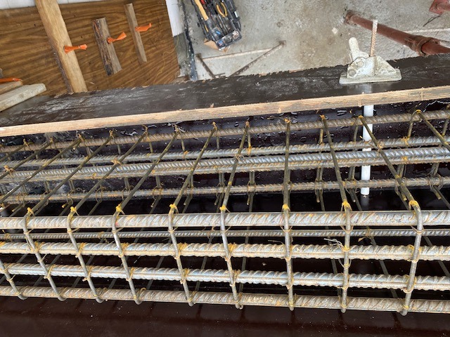 Zbrojenie stalowe ułożone w szalunku z płyty, przygotowane do zalania betonem, widoczne narzędzia i elementy mocujące.