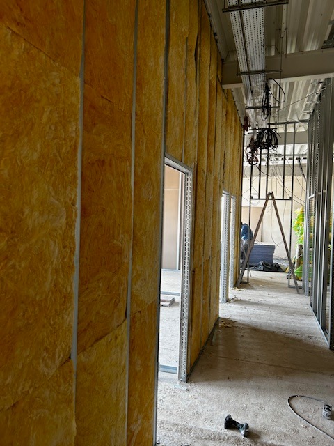 Wnętrze budynku w trakcie izolacji ścian wełną mineralną, widoczne metalowe profile konstrukcyjne i instalacje pod sufitem.