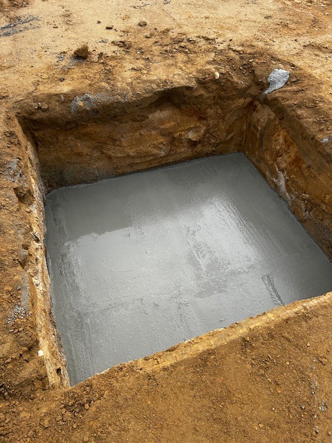 Wykop fundamentowy wypełniony świeżym, gładkim betonem, widok z góry.