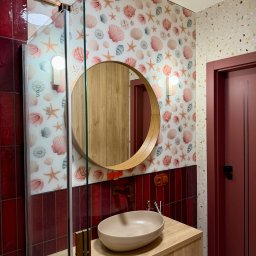 Krzysztof Stachurski Homecraft - Wykończona łazienka z kabiną prysznicową, okrągłym lustrem i umywalką nablatową. Czerwone płytki i tapeta w muszelki dodają unikalnego charakteru.