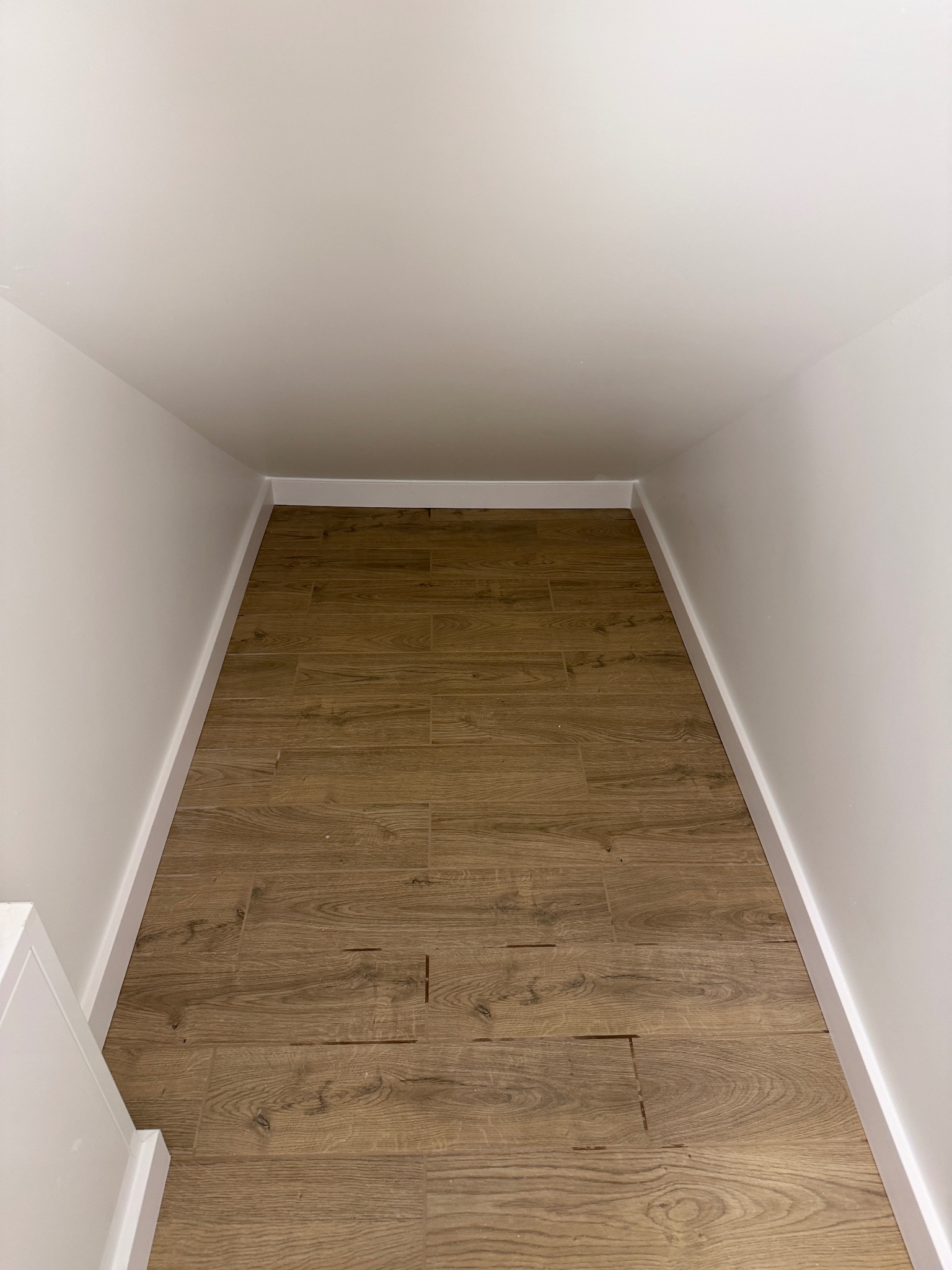 Wykończona wnęka z drewnopodobną podłogą i białymi ścianami. Listwy przypodłogowe w kolorze ścian. Ujęcie z dołu w głąb wnęki.