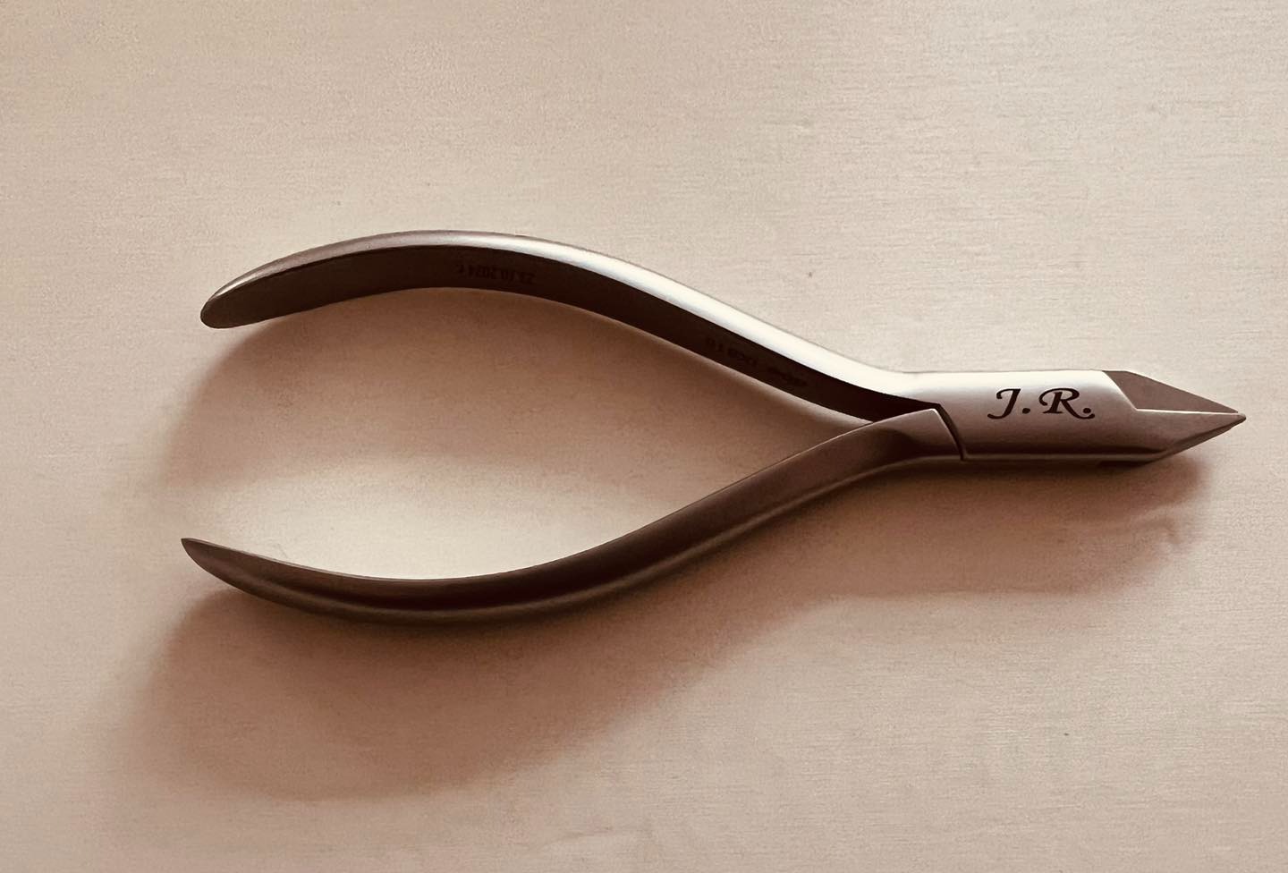 Precyzyjne szczypce ortodontyczne z wygrawerowanymi inicjałami 'J.R.' leżące na gładkiej powierzchni.