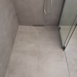 Katarzyna Dublasiewicz - Nowoczesny prysznic walk-in z odpływem liniowym, wykończony szarą, matową glazurą wielkoformatową i szklaną kabiną z chromowanymi okuciami.