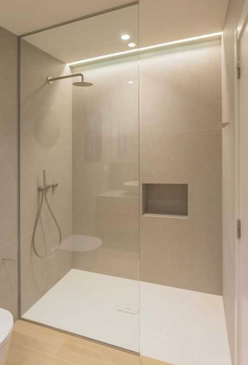 Nowoczesna kabina prysznicowa walk-in z ukrytym oświetleniem LED, wykończona beżowymi płytkami i drewnianą podłogą, z wnęką na kosmetyki.