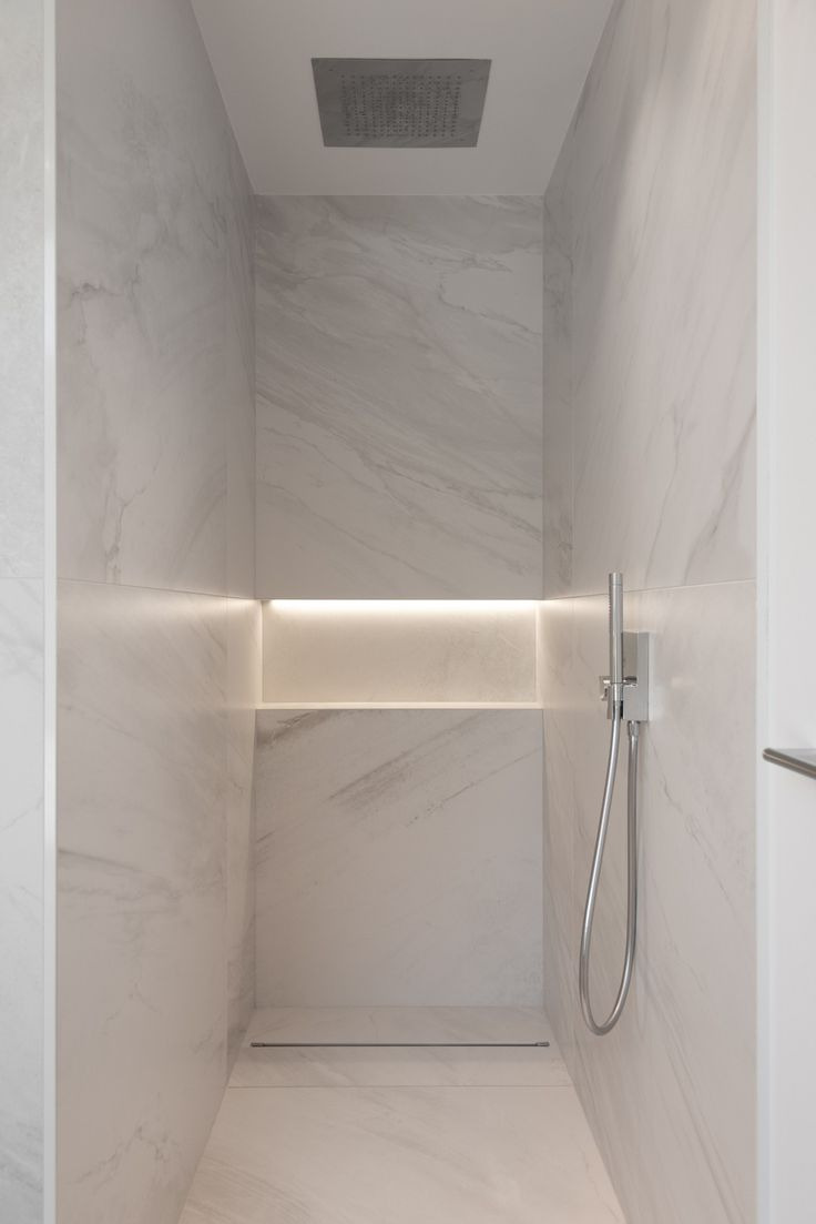 Nowoczesna kabina prysznicowa wyłożona białym marmurem z podświetlaną wnęką i deszczownicą sufitową.