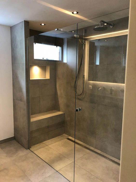 Nowoczesna kabina prysznicowa walk-in z siedziskiem, wykończona szarymi płytkami, oświetleniem punktowym i małym oknem z żaluzją.