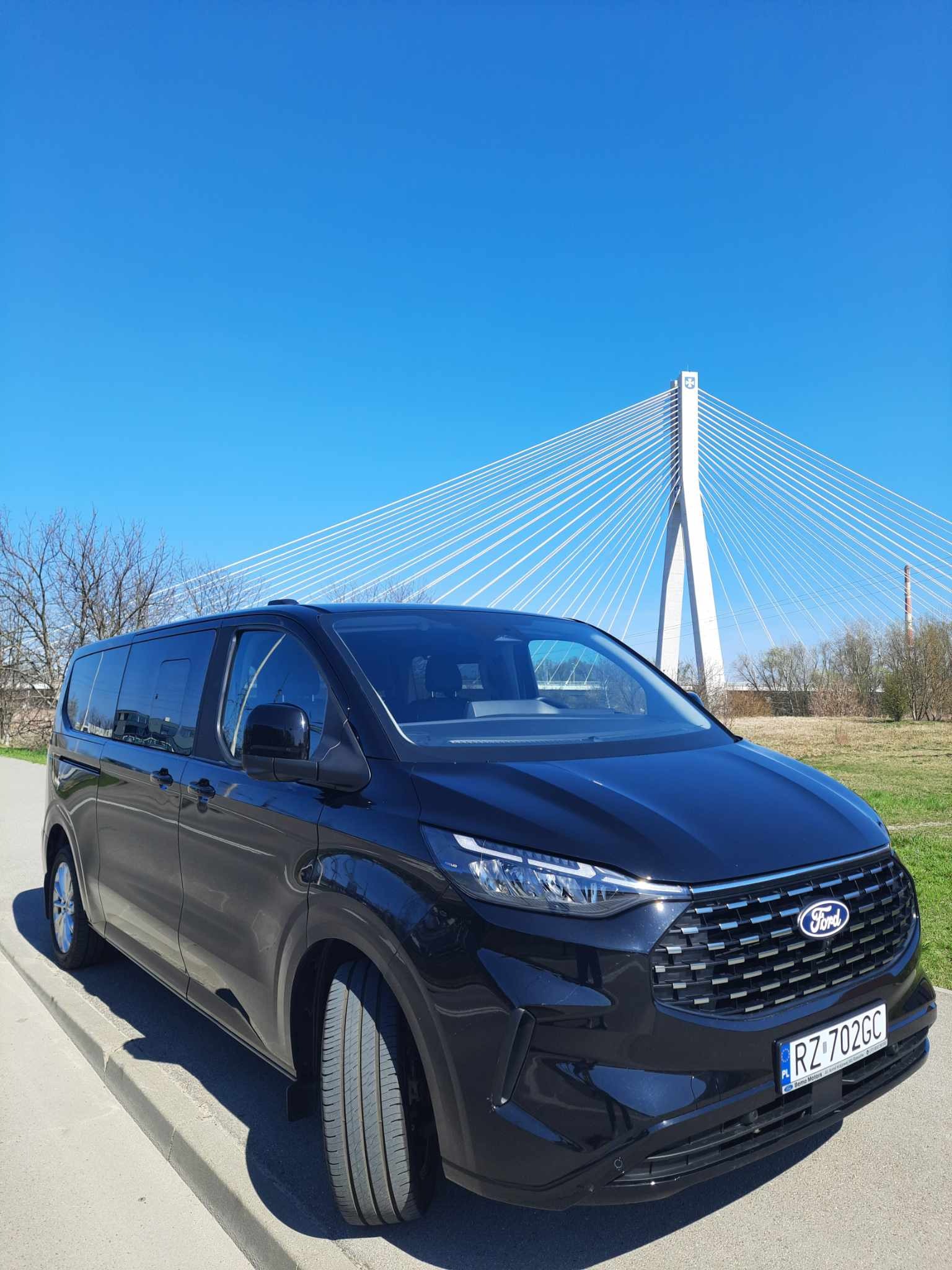 Czarny Ford Transit Custom z widocznym numerem rejestracyjnym RZ 702GC, na tle mostu wantowego i błękitnego nieba.