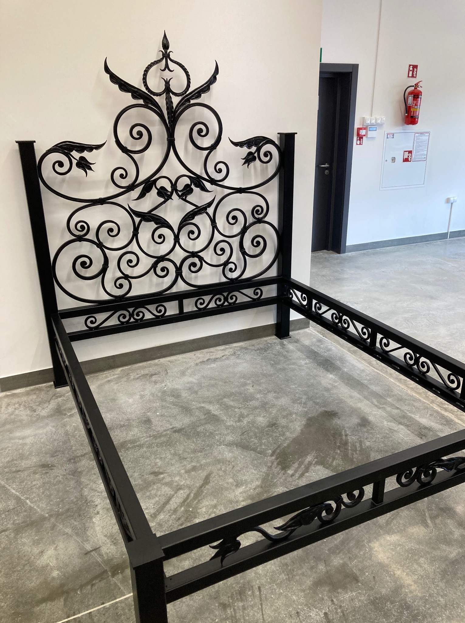 Stelaż łóżka z metaloplastyki w Zakopanem, z dekoracyjnym wezgłowiem i ramą, czarne wykończenie, surowe wnętrze.