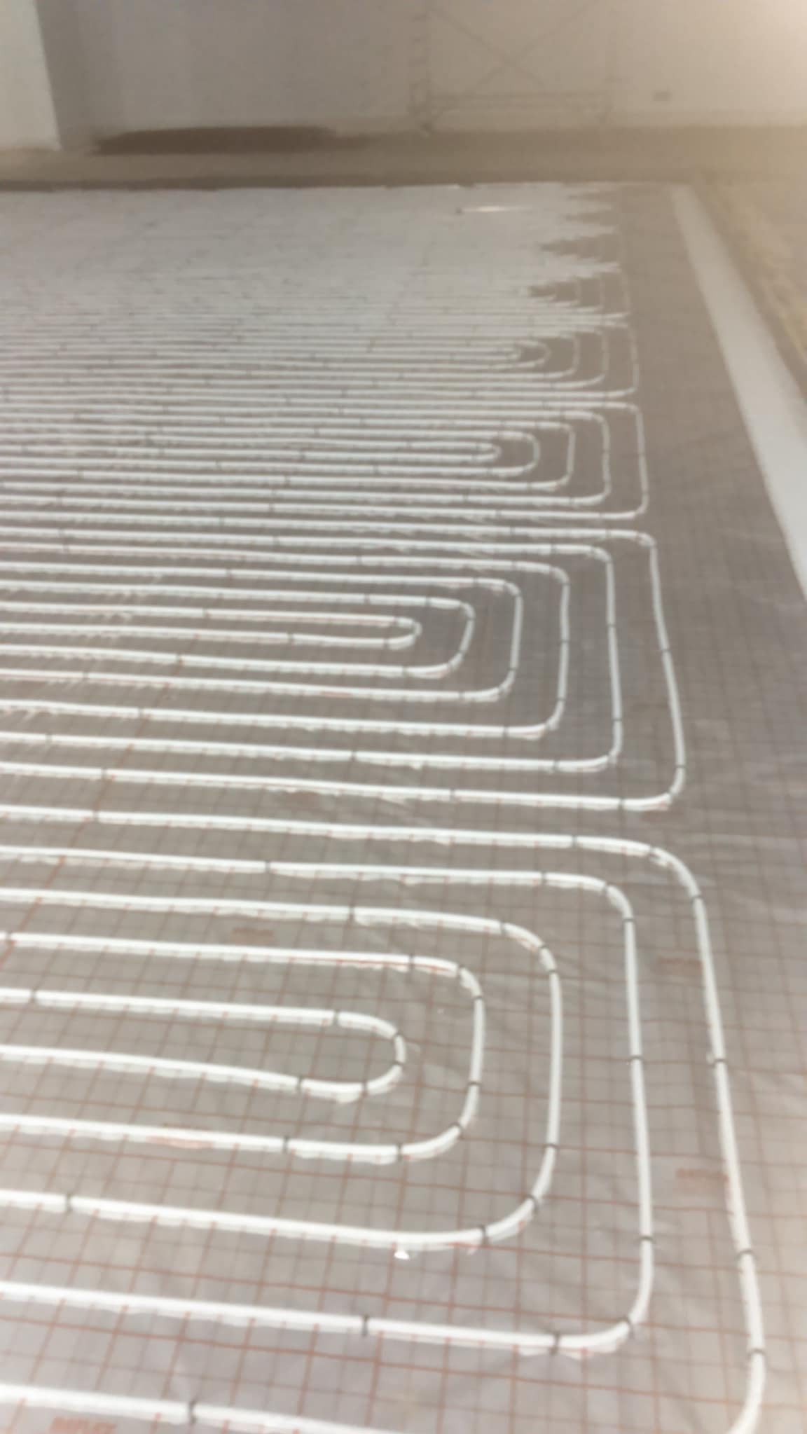 Białe rurki ogrzewania podłogowego ułożone w pętle na siatce montażowej, widok z góry, surowy stan przed wylaniem posadzki.