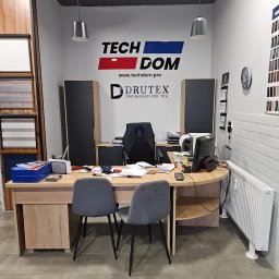 TECH-DOM S.C. JAROSŁAW BUSZKA DARIUSZ DARGACZ - Biuro firmy Tech Dom Drutex z ekspozycją próbek okien i rolet, widoczne biurko, krzesła, komputer i materiały biurowe.