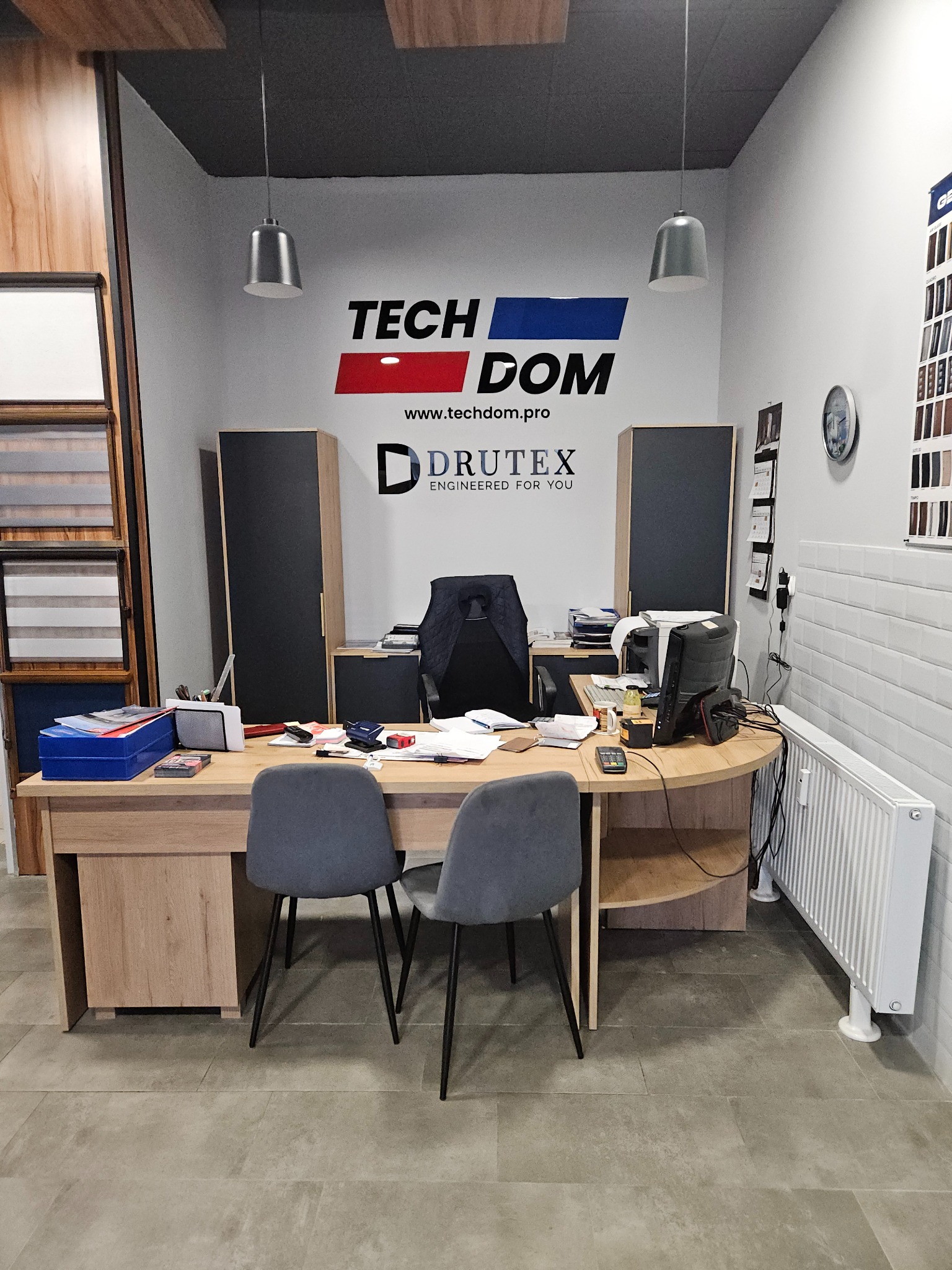 Biuro firmy Tech Dom Drutex z ekspozycją próbek okien i rolet, widoczne biurko, krzesła, komputer i materiały biurowe.