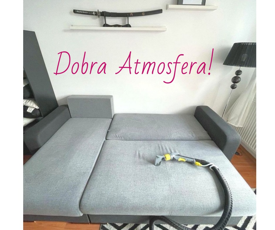 Szara rozkładana sofa podczas czyszczenia z użyciem ssawki ekstrakcyjnej; w tle biała ściana z dekoracyjną kataną na półce i lampą podłogową.