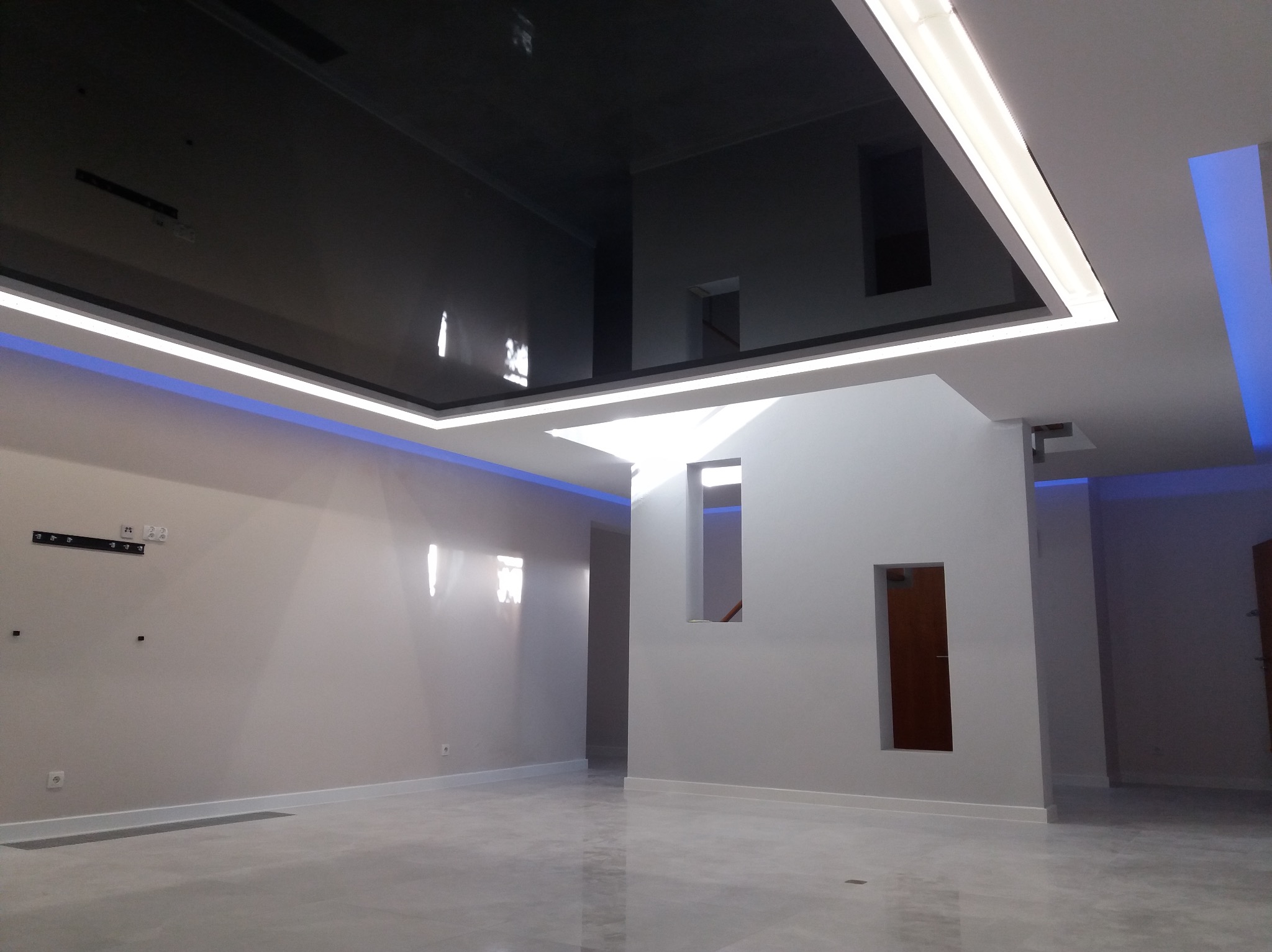 Nowoczesne wnętrze z podwieszanym, lustrzanym sufitem i oświetleniem LED, minimalistyczny design z drzwiami osadzonymi w ścianie.