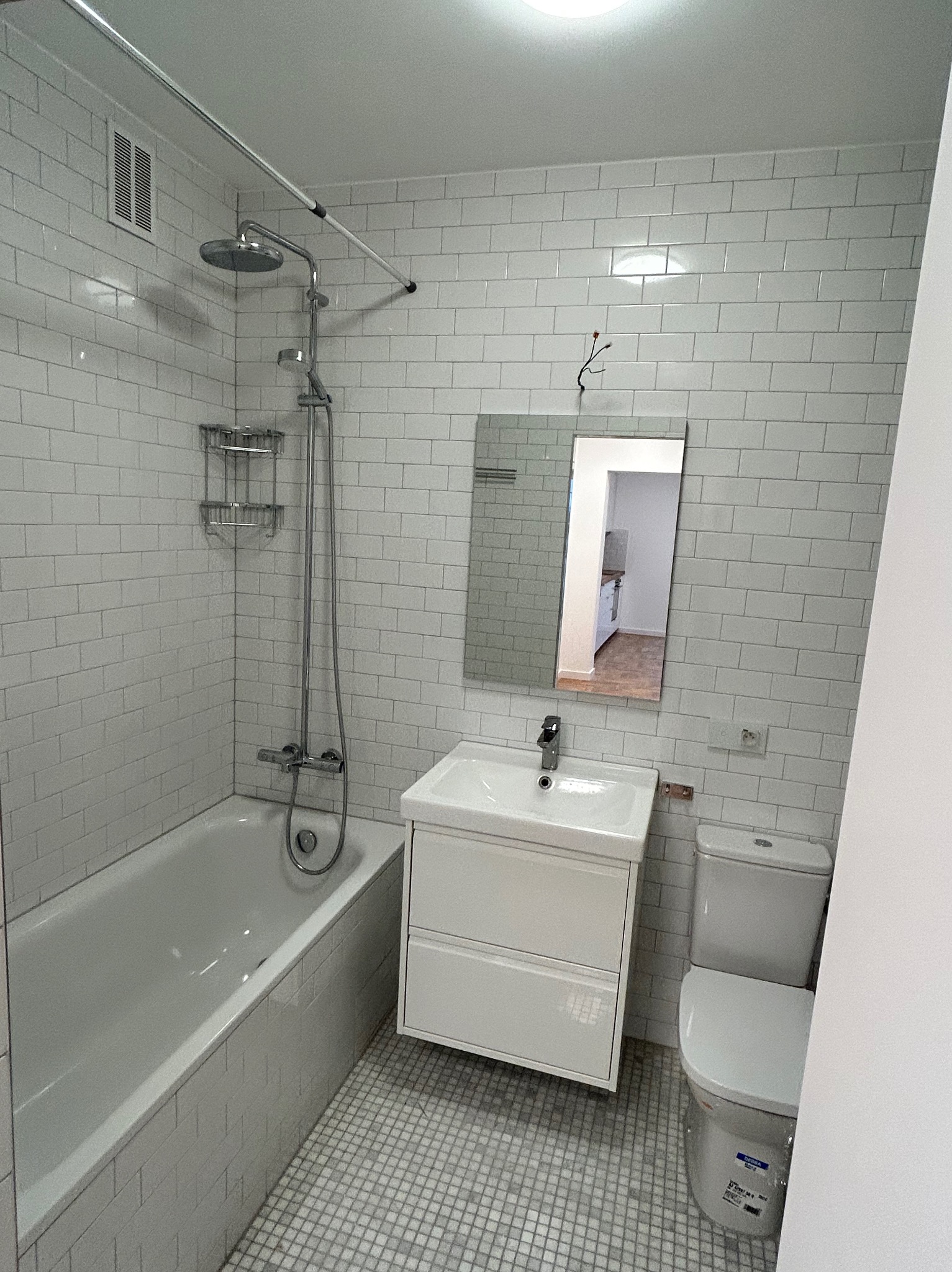 Wykończona łazienka w Legnicy z białą armaturą, kabiną prysznicową nad wanną, umywalką z szafką i toaletą, wyłożona białymi płytkami typu metro i mozaikową podłogą.