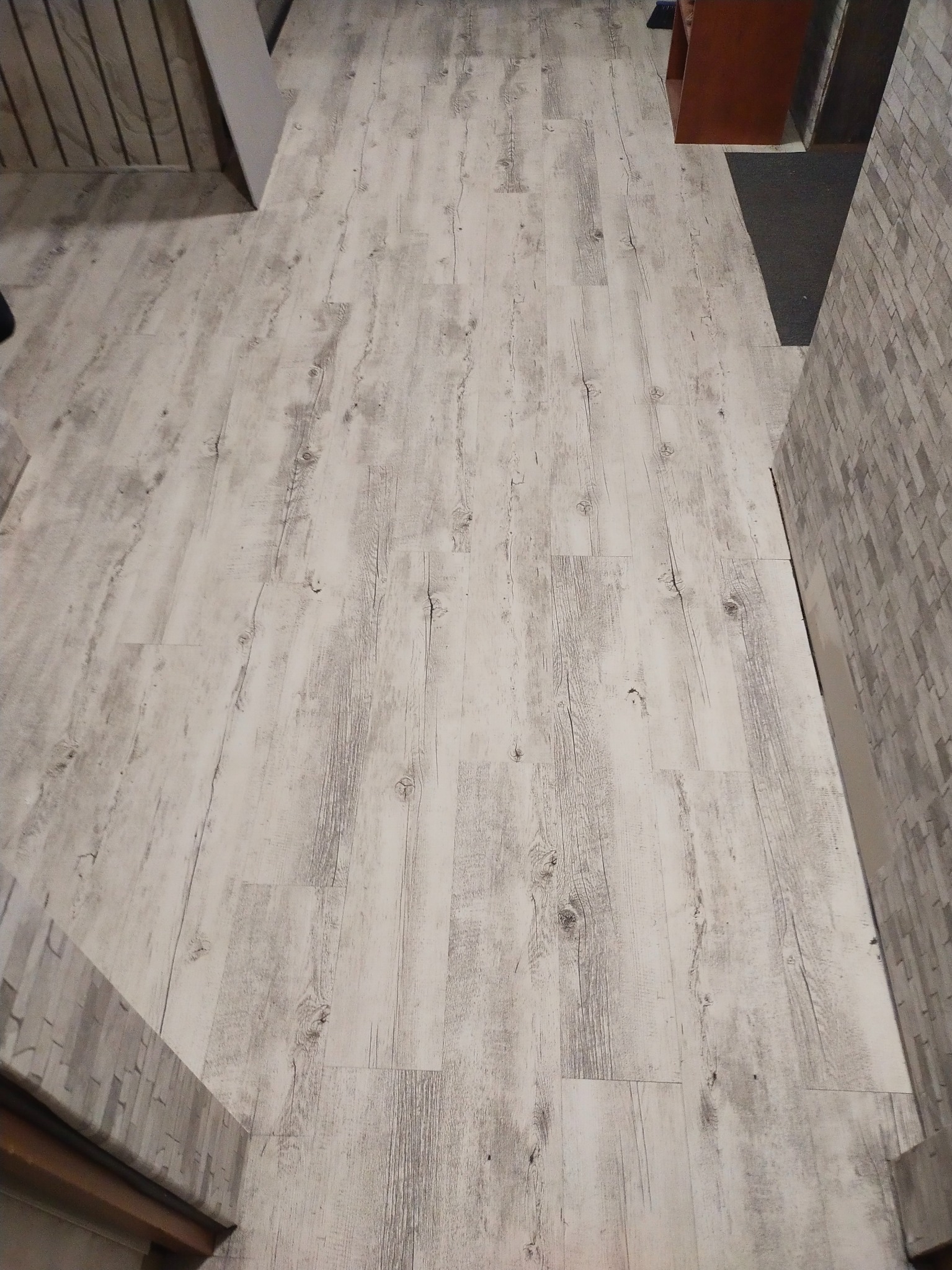 Ułożona podłoga z paneli imitujących bielone drewno, widok z góry, fragment ściany z szarej cegły dekoracyjnej po prawej stronie.