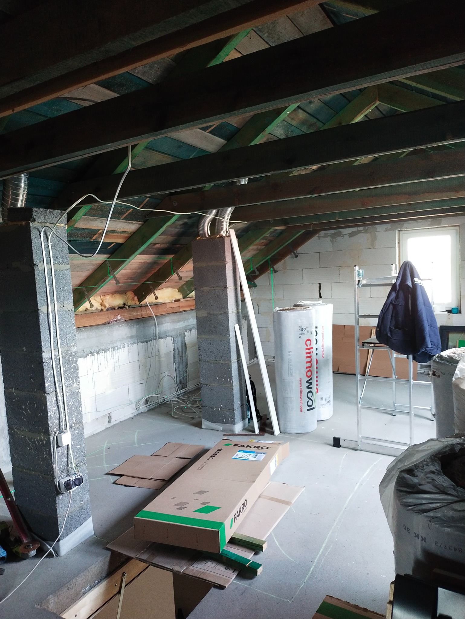 Poddasze w trakcie adaptacji: widoczne ocieplenie, elementy konstrukcyjne, kartony z oknami dachowymi Fakro, instalacje elektryczne i wentylacyjne.