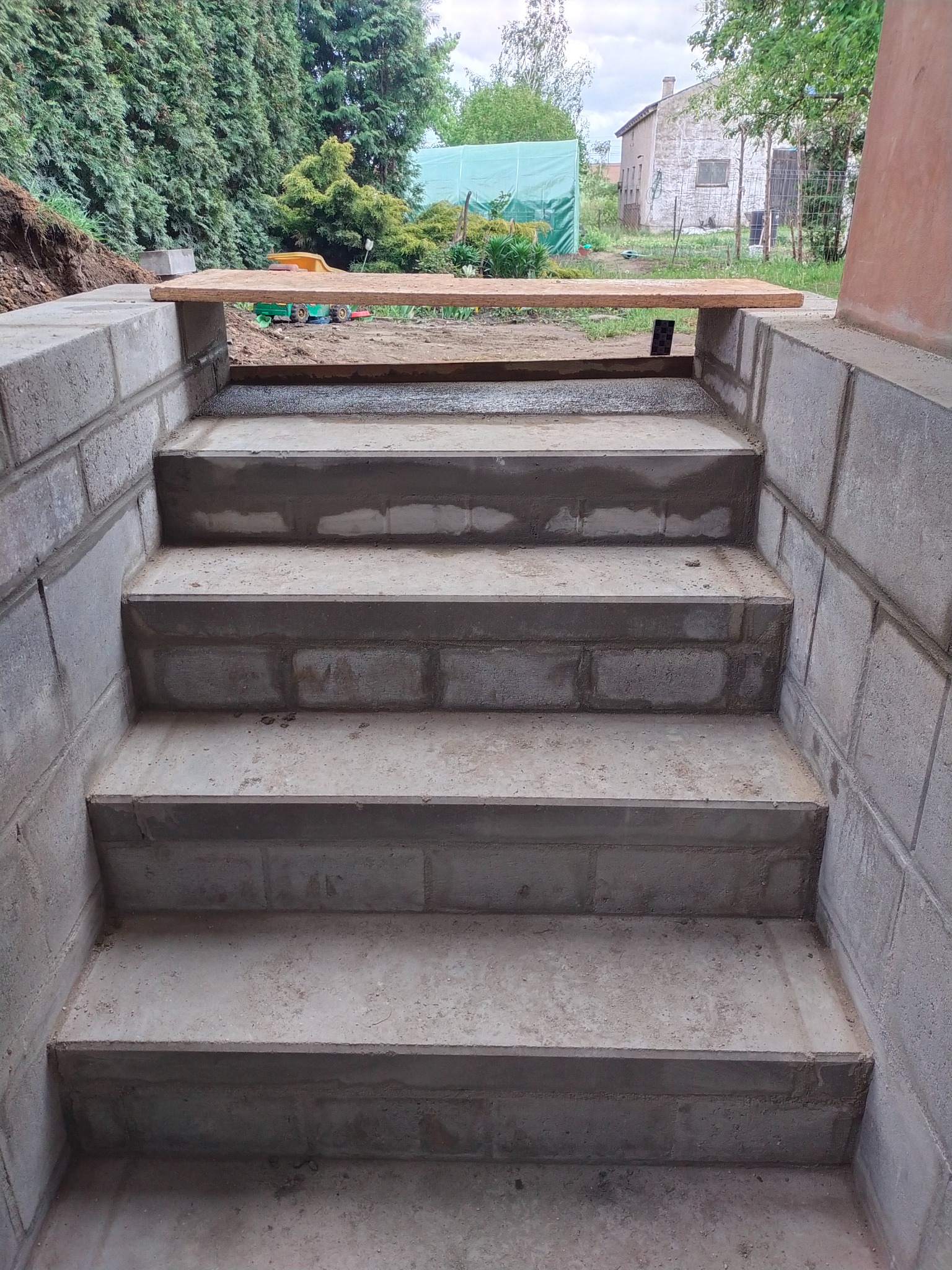 Betonowe schody zewnętrzne w trakcie budowy, z widocznymi bloczkami betonowymi i śladami zaprawy, na tle zieleni i budynku.