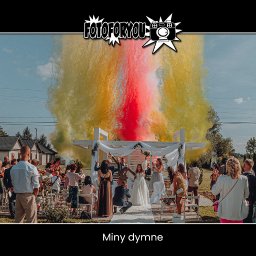 FotoForYou Atrakcje eventowe - Para młoda świętuje pod białym, drewnianym baldachimem, otoczona gośćmi weselnymi, z wybuchami kolorowego dymu w odcieniach czerwieni i żółci w tle, nad nimi logo fotografa.