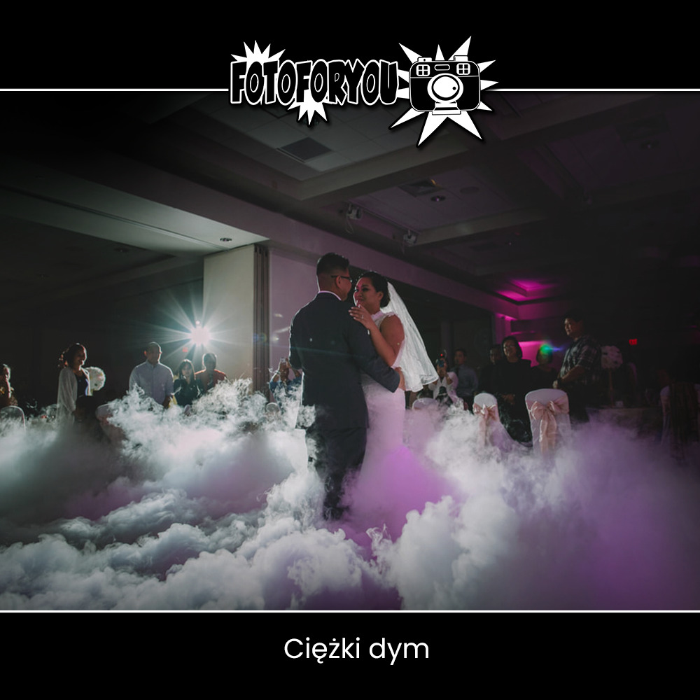 Para młoda tańczy pierwszy taniec w sali weselnej, otoczona ciężkim dymem podświetlonym na fioletowo, widoczny zespół i goście weselni w tle, logo fotografa w górnej części zdjęcia.
