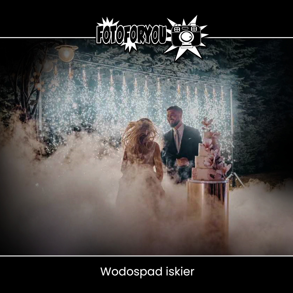 Para młoda stoi obok tortu weselnego podczas pokazu fajerwerków na zewnątrz, widoczna mgła i iskry.