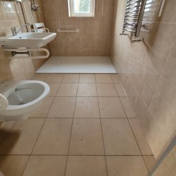 GLAZURA USŁUGI REMONTOWO-BUDOWLANE TOMASZ SZWEDO - Beżowa łazienka z białą umywalką na regulowanej wysokości z poręczami, toaletą, brodzikiem bezprogowy i grzejnikiem drabinkowym