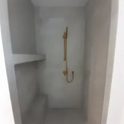 Minimalistyczna kabina prysznicowa w odcieniach szarości z złotą armaturą i półką wnękową.