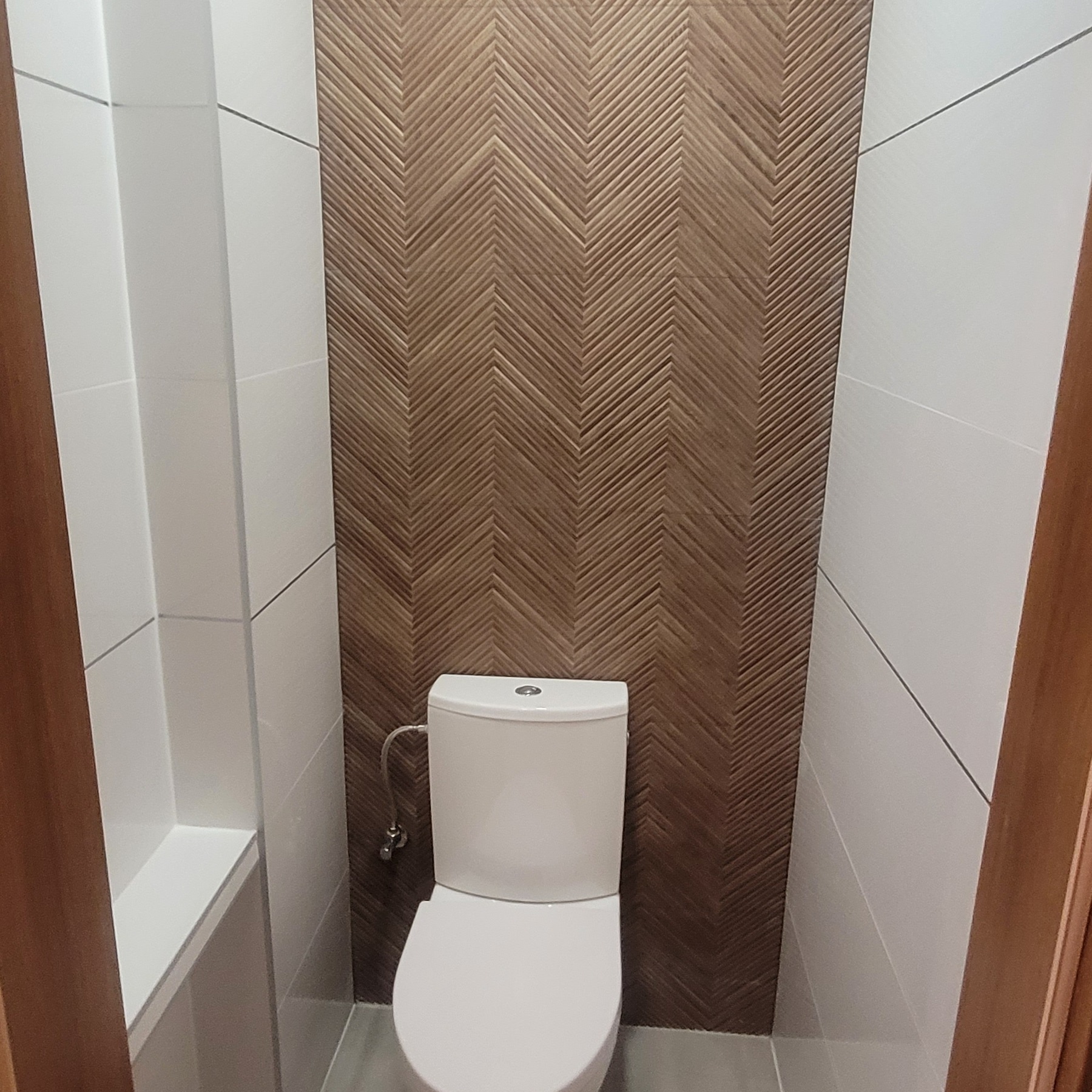 Nowoczesna łazienka z białą ceramiką i dekoracyjną ścianą z drewnopodobnych paneli ułożonych w jodełkę, białe płytki na pozostałych ścianach.