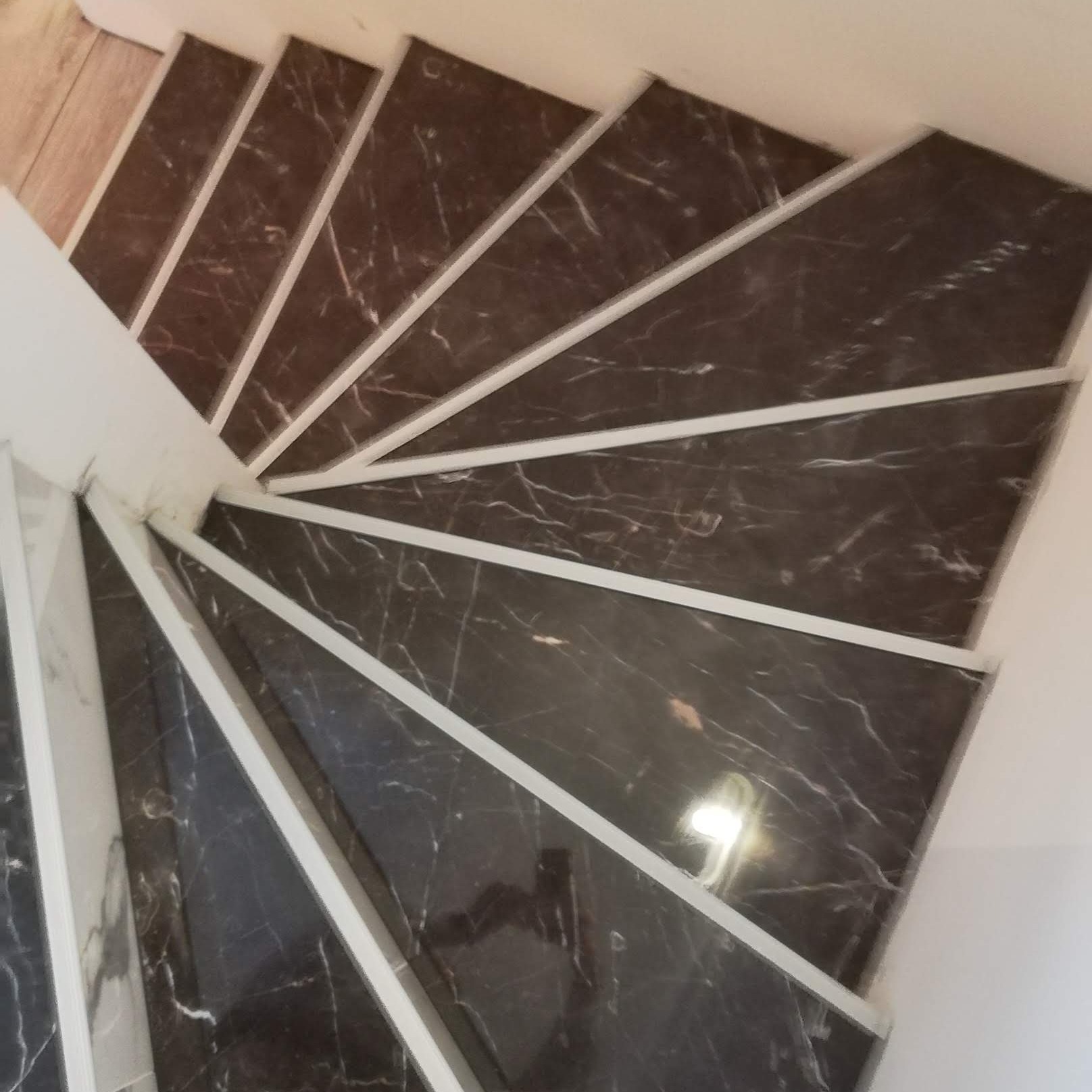 Widok z góry na spiralne schody wyłożone ciemnym marmurem z białymi żyłkami, oddzielone białymi listwami.