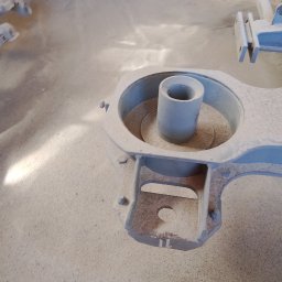 Tynki Maszynowo - Gipsowe Paweł Okoński - Szara, odlewana forma z cylindrycznym otworem i numerem '1L' na podstawie, otoczona piaskiem odlewniczym.