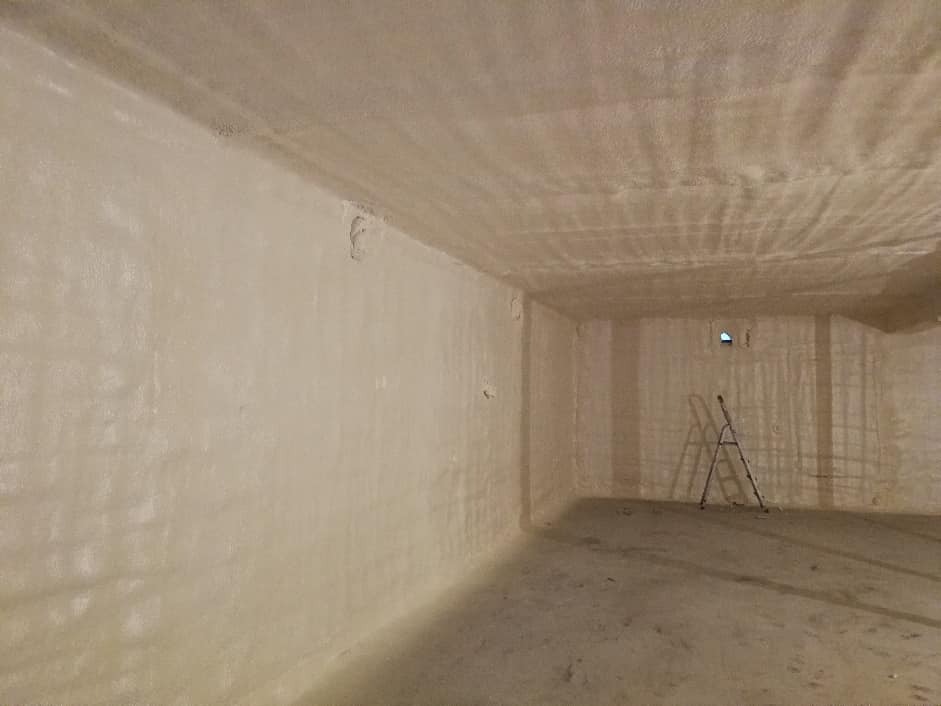 Poddasze po ociepleniu pianką poliuretanową, widoczna struktura natrysku na ścianach i suficie, drabina oparta o ścianę w tle.