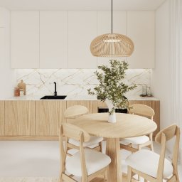 Poukładane Justyna Tarasiewicz - Jasna kuchnia z drewnianymi akcentami: okrągły stół z krzesłami, marmurowy backsplash, wisząca lampa z naturalnego materiału i delikatne, białe zasłony przy oknie.