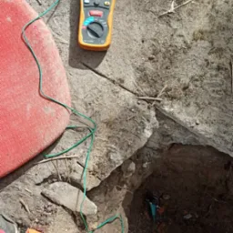 Miernik elektryczny wyświetlający pomiar 6.42, z przewodami podłączonymi do gruntu, obok leży zwój przewodów i młotek