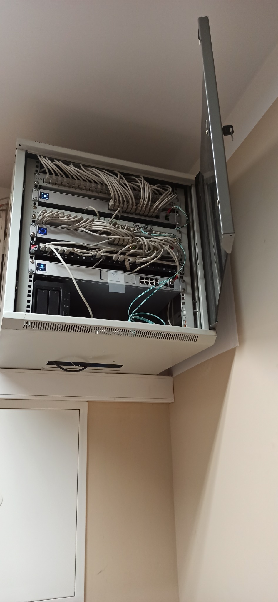 Szafa rack z zamontowanym sprzętem sieciowym, widoczne kable patchcord, urządzenia sieciowe i otwarte drzwi szafy z kluczykiem.