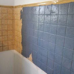 Centrum Napraw Domowych - Malowanie płytek w łazience na kolor szary, widoczne fragmenty starej, beżowej glazury i taśma malarska zabezpieczająca krawędzie.