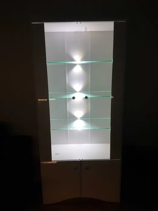 Podświetlana witryna z szklanymi półkami i dolnymi szafkami, widoczna w ciemnym otoczeniu.