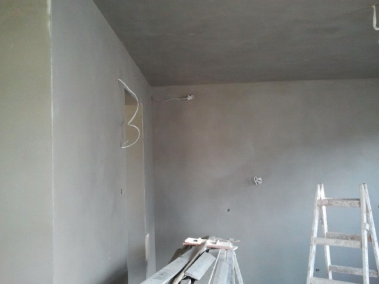 Świeżo otynkowane wnętrze z widoczną drabiną i wystającymi przewodami elektrycznymi, przygotowane do dalszych prac wykończeniowych.