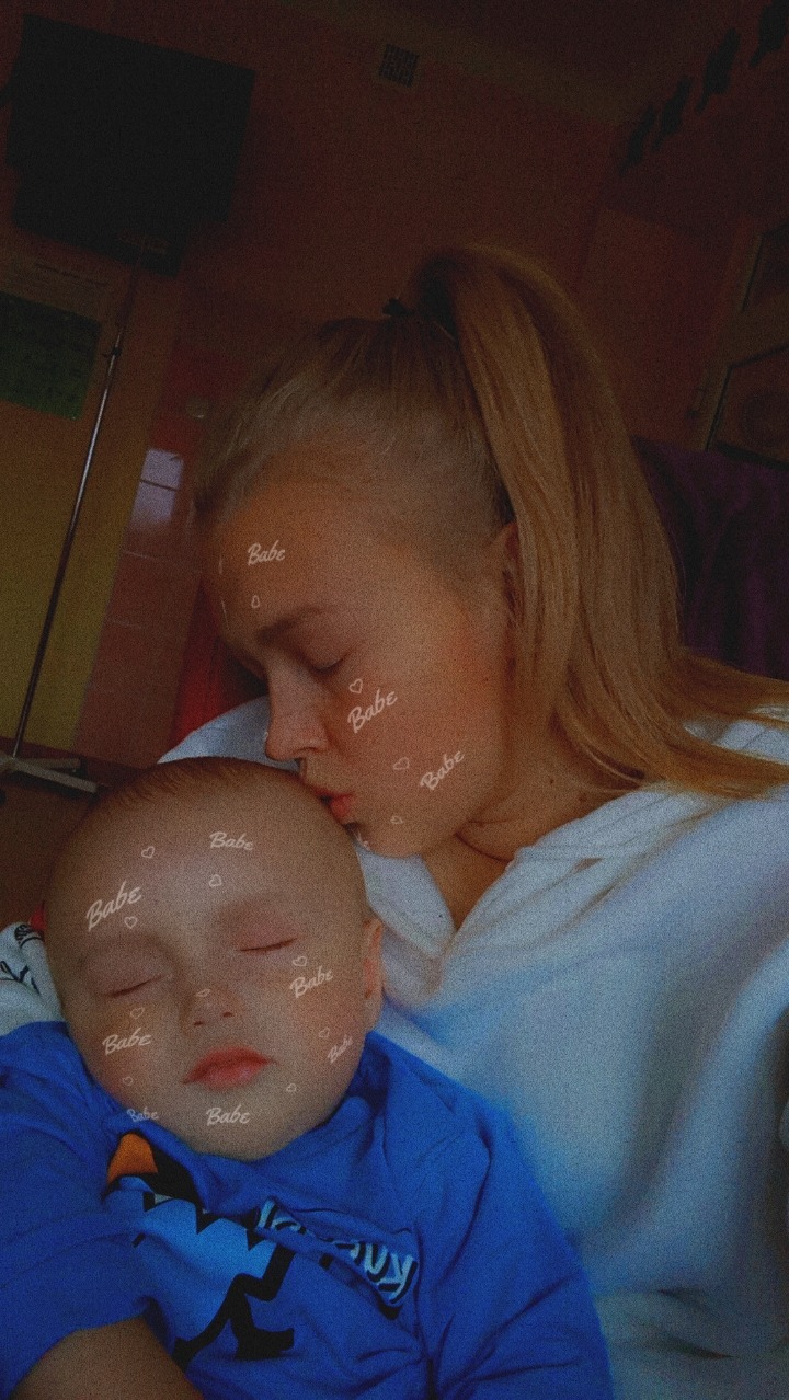 Blondwłosa kobieta całuje w czoło śpiącego chłopca w niebieskiej koszulce, oboje z filtrem 'Babe' na twarzach.