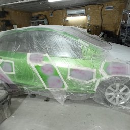 L&M DESIGN - Przygotowanie do lakierowania: zielony samochód oklejony taśmą i folią ochronną, widoczne szpachlowane fragmenty karoserii.