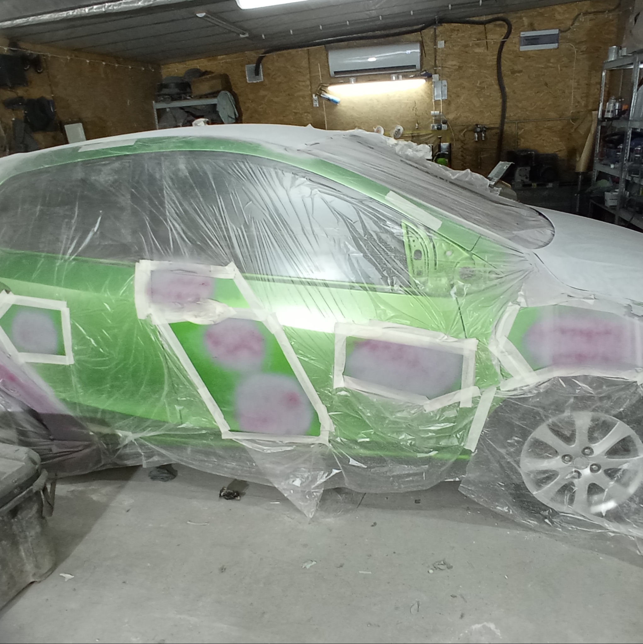 Przygotowanie do lakierowania: zielony samochód oklejony taśmą i folią ochronną, widoczne szpachlowane fragmenty karoserii.