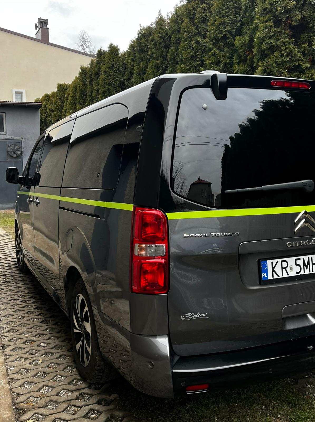 Szary Citroen SpaceTourer z zielonym pasem, widok z tyłu na tle zielonych drzew i budynku. Tablica rejestracyjna z Polski.