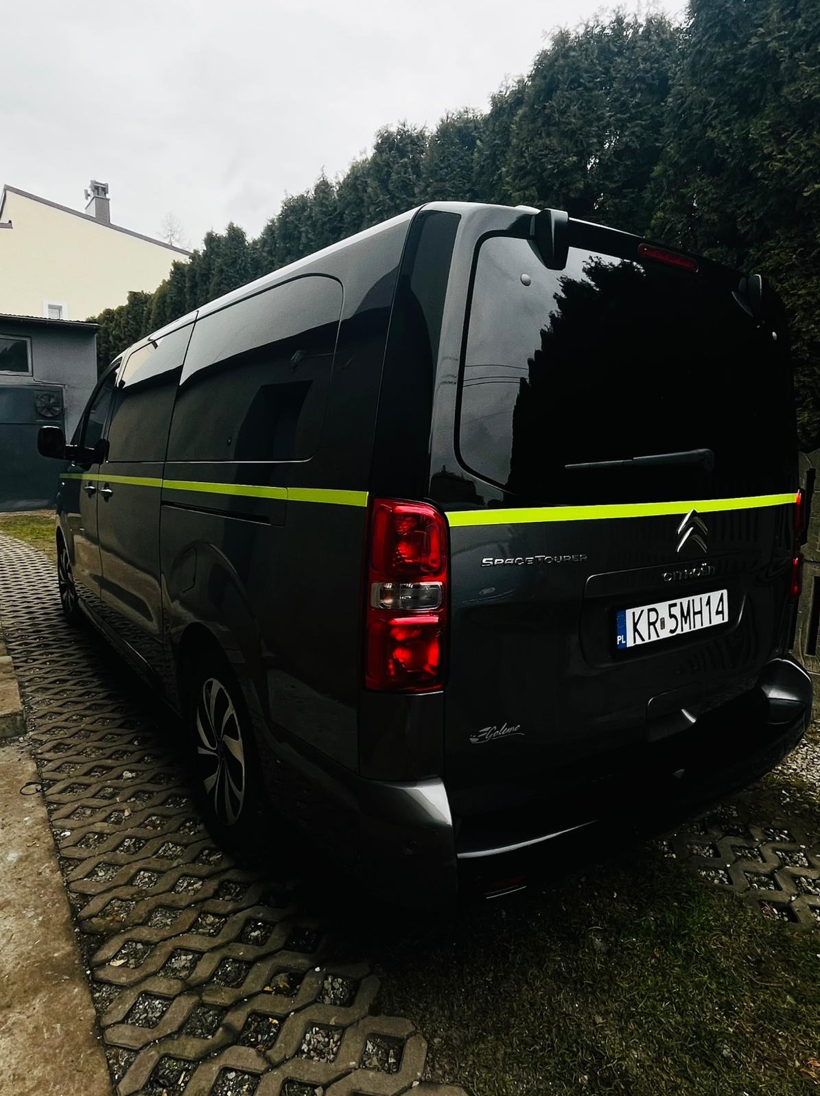 Czarny Citroen SpaceTourer z żółtym pasem, widok z tyłu na tle zielonych drzew i budynku, tablica rejestracyjna KR 5MH14.