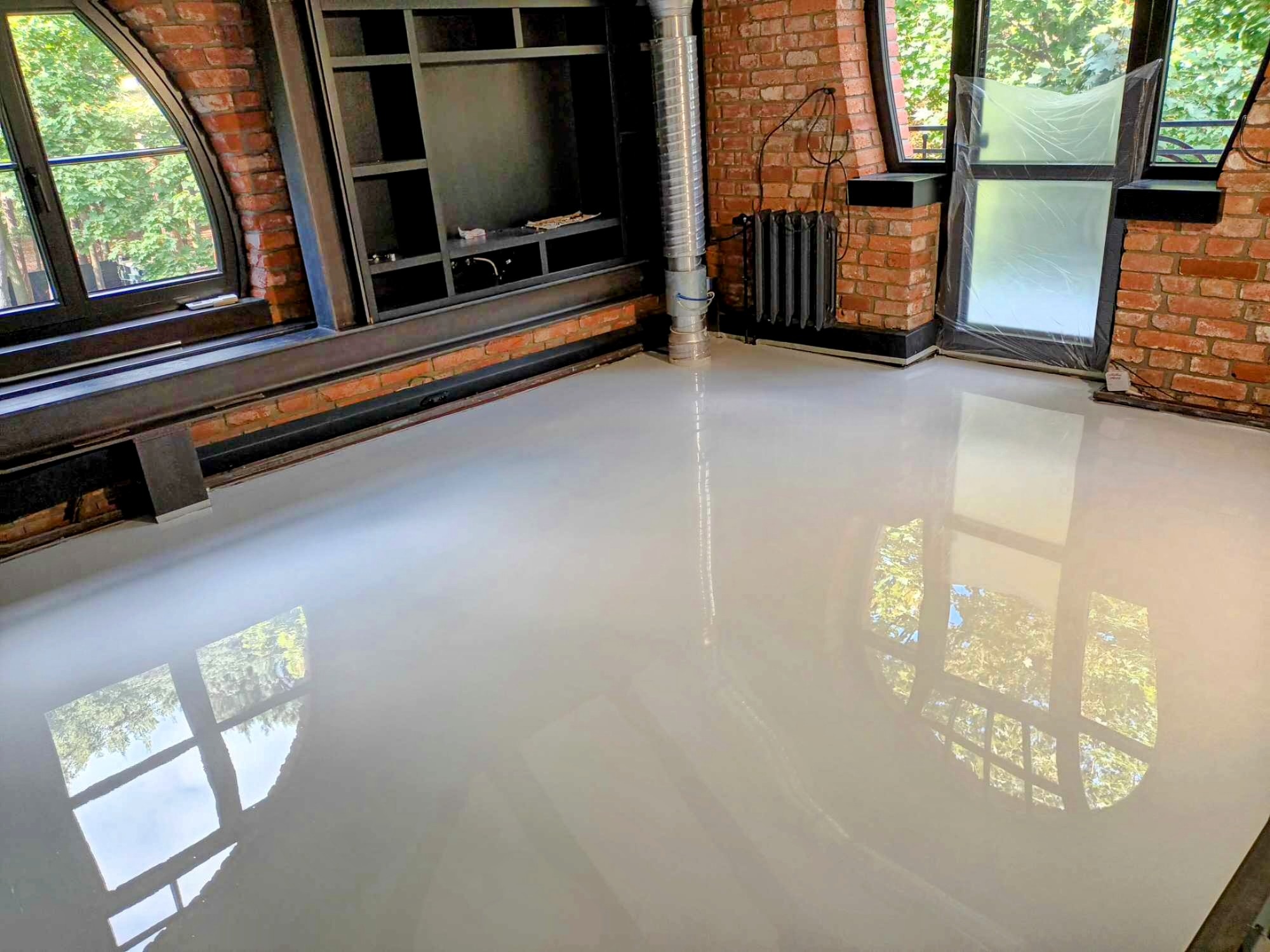 Jasna, gładka posadzka z odbiciem okien w pokoju z ceglanymi ścianami i czarnymi ramami okiennymi o nietypowym kształcie.