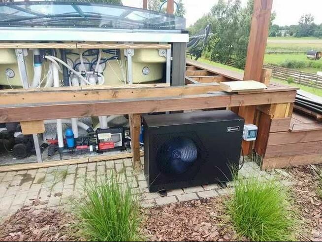 Instalacja basenu z widocznym systemem filtracji, pompą ciepła i drewnianą konstrukcją nośną, otoczona zielenią i częściowo wykończona drewnianym tarasem.